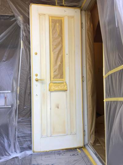 塗料が付着しないよう、ガラス部分や周囲の壁などをマスキングテープとビニールシートで丁寧に養生している様子