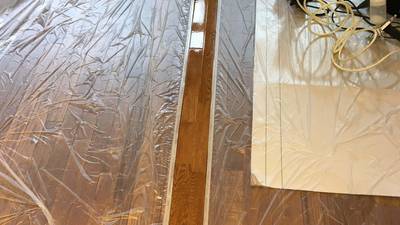 周囲を養生し、スプレーガンを使って新しいフローリング板に色を乗せている塗装作業中の様子