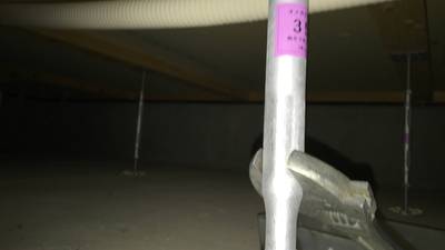 薄暗い床下空間で、大引きを支えている鋼製束の上部をスパナを使って調整している様子