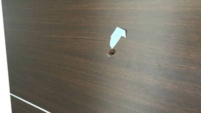 ダークブラウンの木目調引き戸に空いた、表面シートがめくれ上がった穴